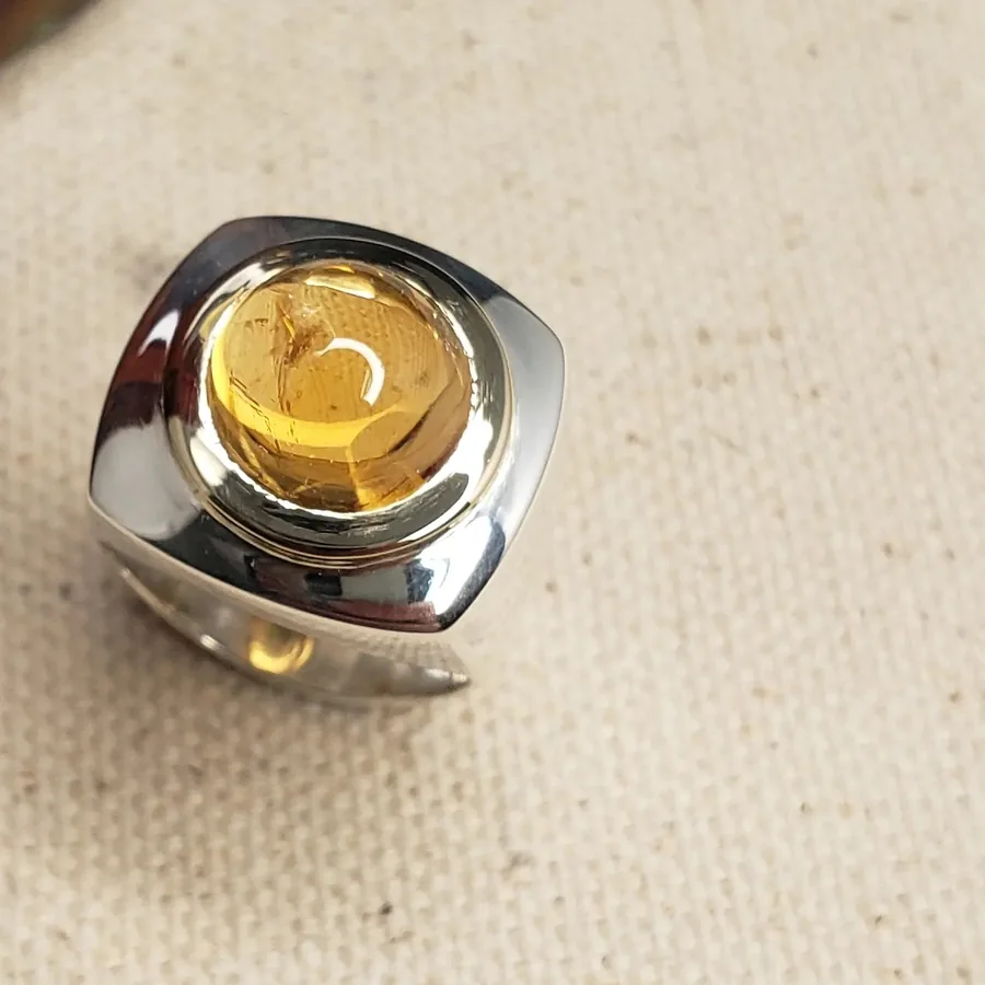 A chunky silver ring holding a domed golden citrine cabochon, on cream woven fabric.