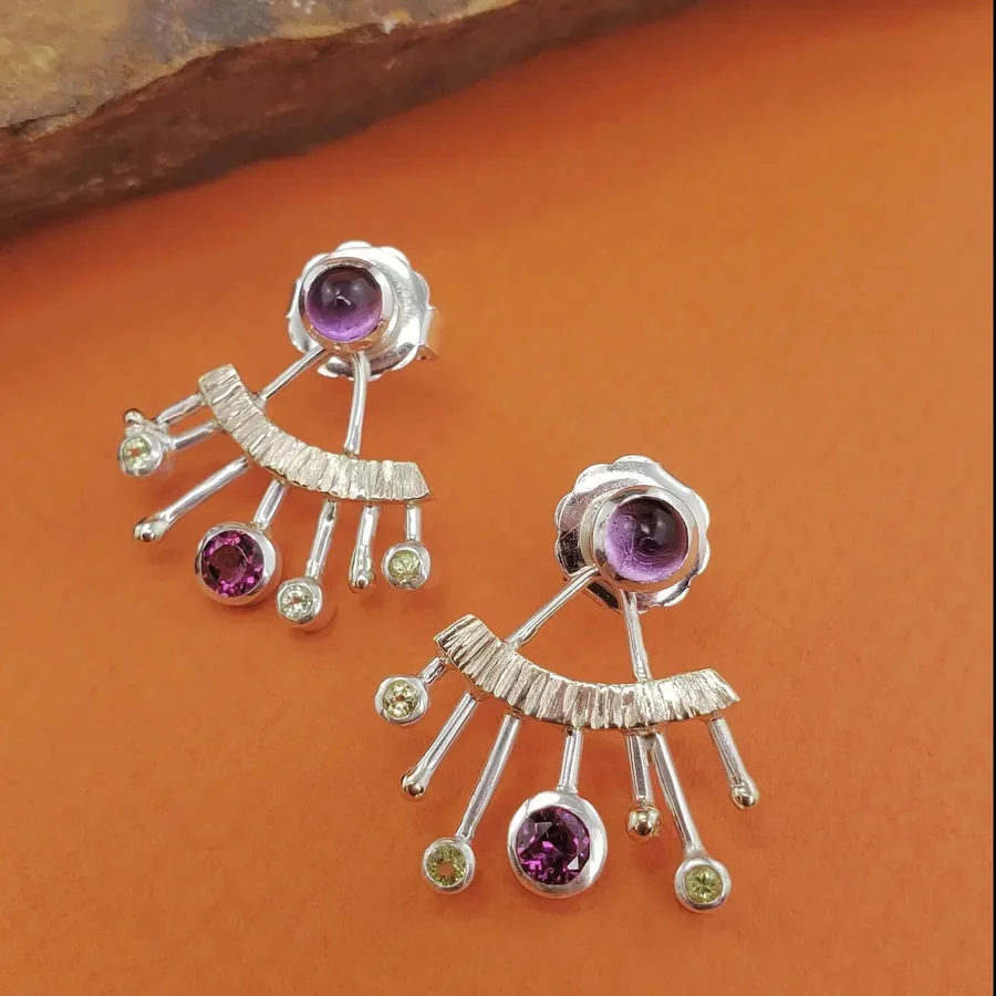 An asymmetric starburst earring in mixed gold and silver, tipped with amethyst, garnet and peridot.