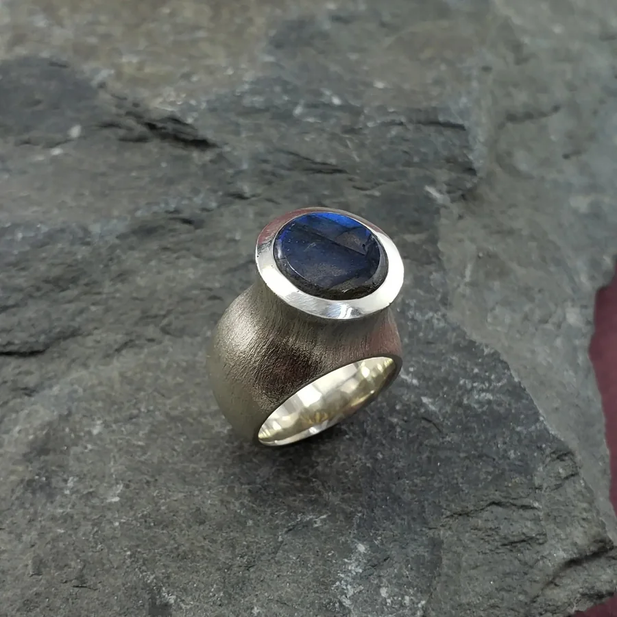 A brushed silver tower ring set with an oval labradorite cabochon, on slate.
