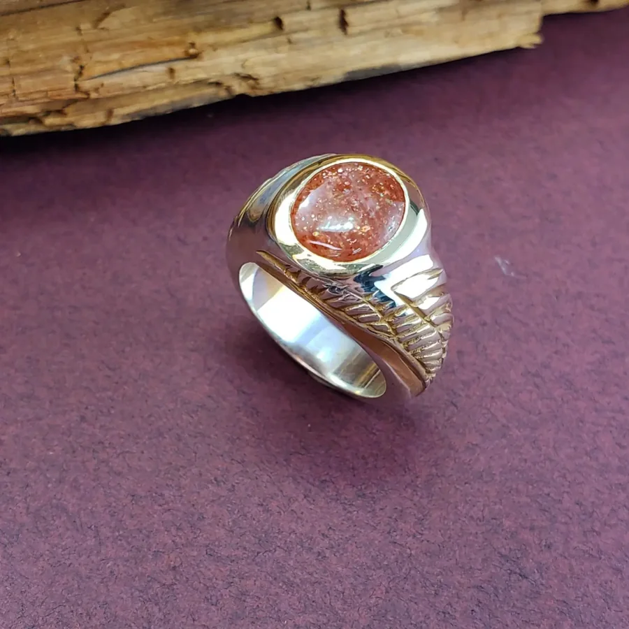 A silver ring set with a sunstone feldspar, with golden wings carved into the sloping sides.