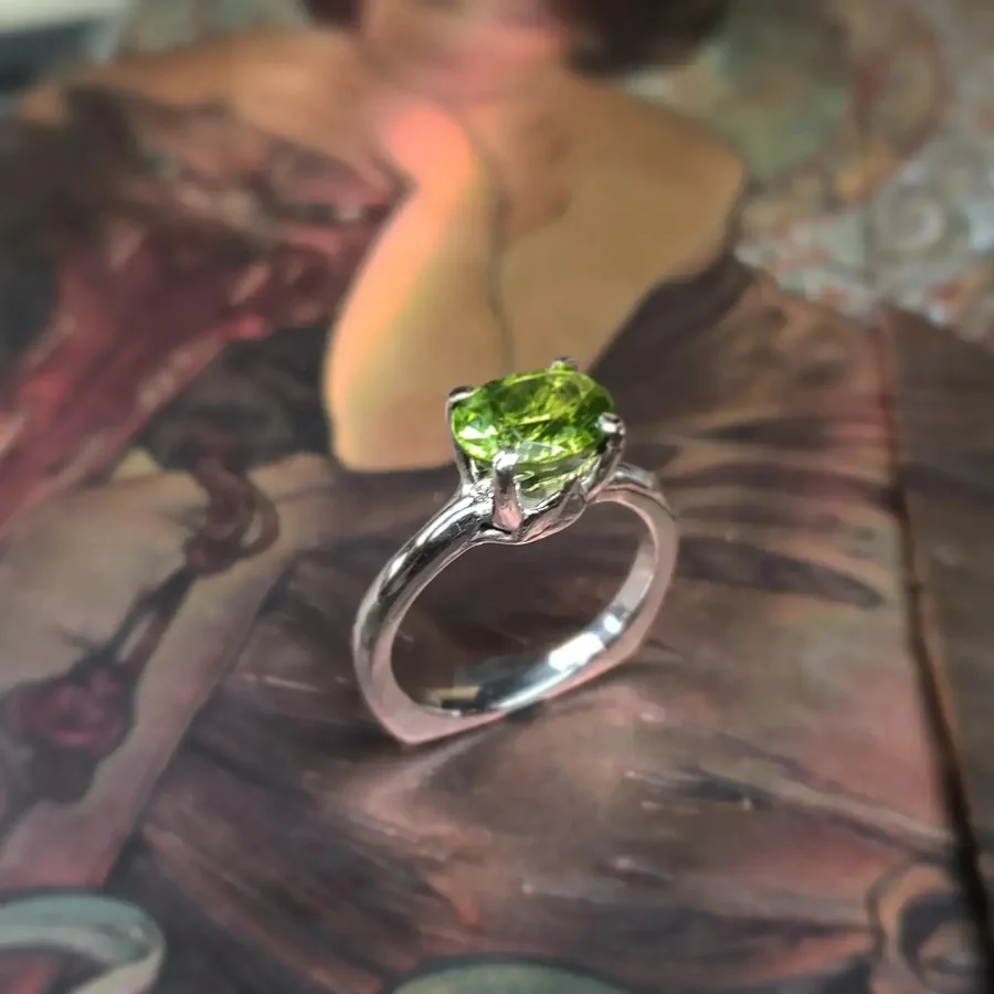A silver ring set with a large round peridot, resting on a printed art book.